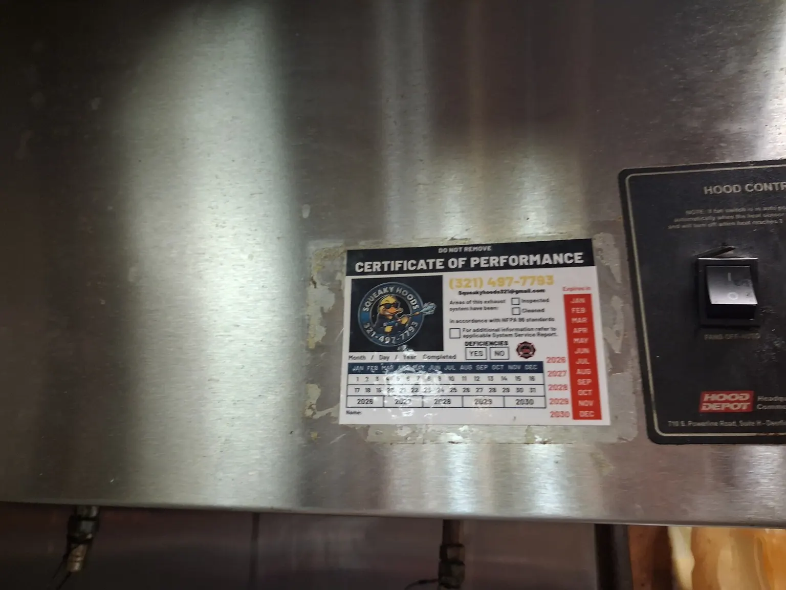 A Certificate of Performance sticker on the stainless steel of a cleaned hood, carrying the Squeaky Hoods badge, a phone number, and the line “in accordance with NFPA 96 standards”.