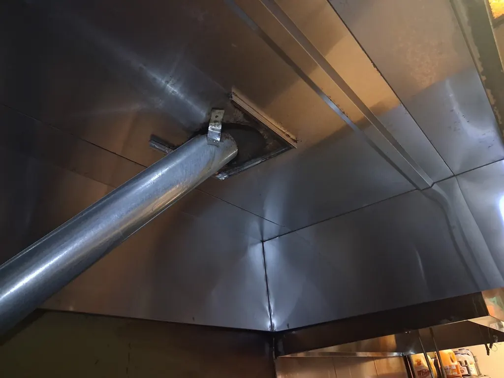 The duct collar in the top of a commercial kitchen hood after cleaning, with the ductwork running away above it and bare metal around the opening.