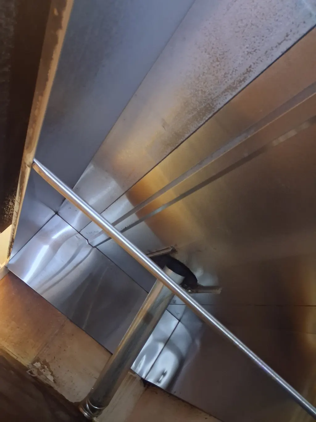 Looking up into the inside of a commercial kitchen hood after cleaning, the plenum and its baffles down to bare stainless metal.